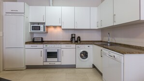 Een moderne keuken met witte kasten, een magnetron, een koffiezetapparaat, een oven, een wasmachine en een vaatwasser.