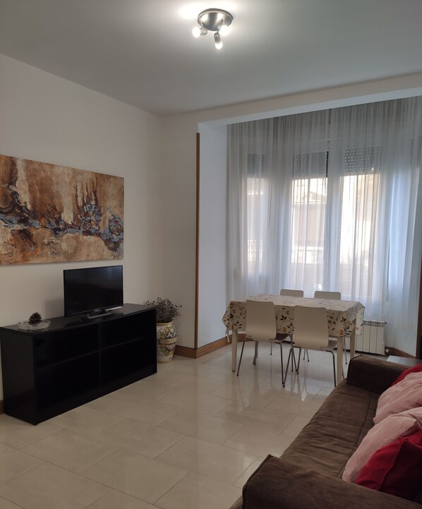 A living room with a flat-screen TV on a black stand, a dining table with chairs, a brown sofa, and a large abstract painting on the wall. - ZURRIOLA SURF BEACH. Optional parking. ESS00856 (Donostia)
