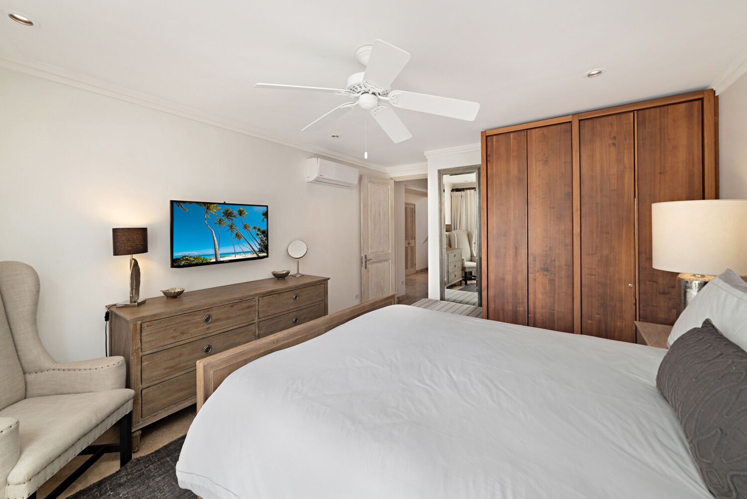 A bedroom with a bed, a wooden dresser, a chair, a television, and a ceiling fan.