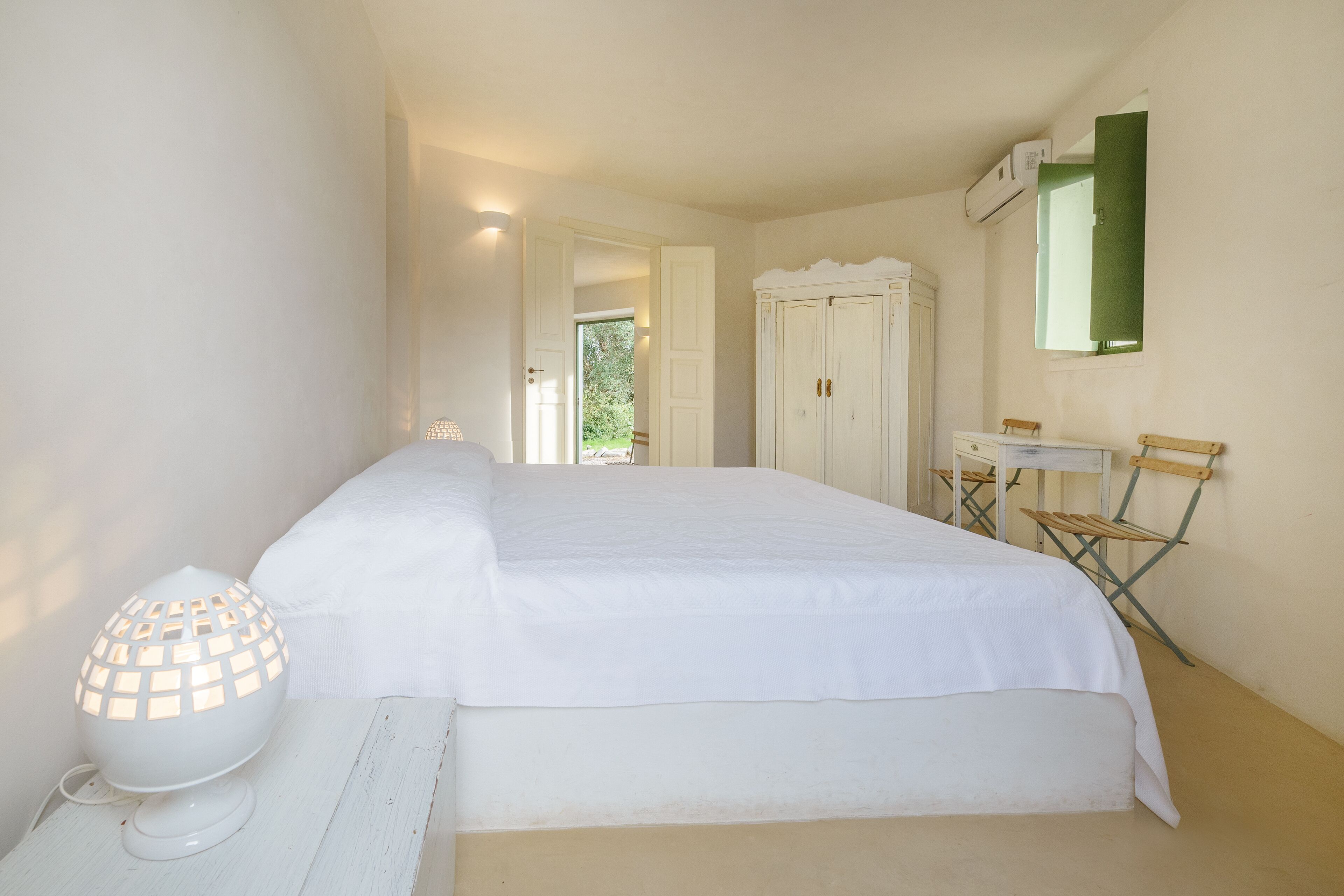 Ein Schlafzimmer mit einem Bett, einer Nachttischlampe, einem Kleiderschrank, einem Spiegel und einem Fenster.
