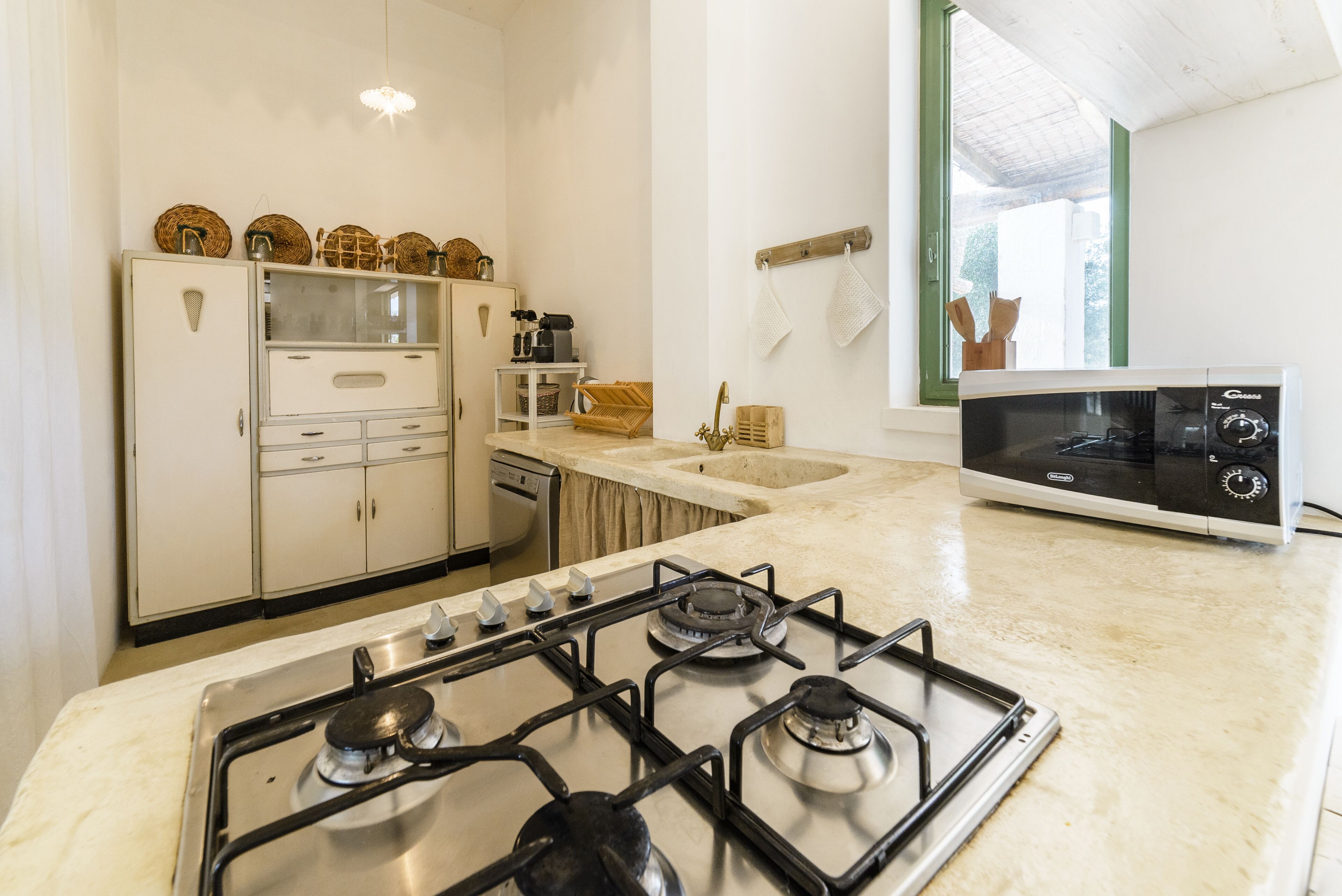 Une cuisine équipée d’une cuisinière à gaz, de meubles blancs, d’un four à micro-ondes et d’une fenêtre donnant sur un espace verdoyant.