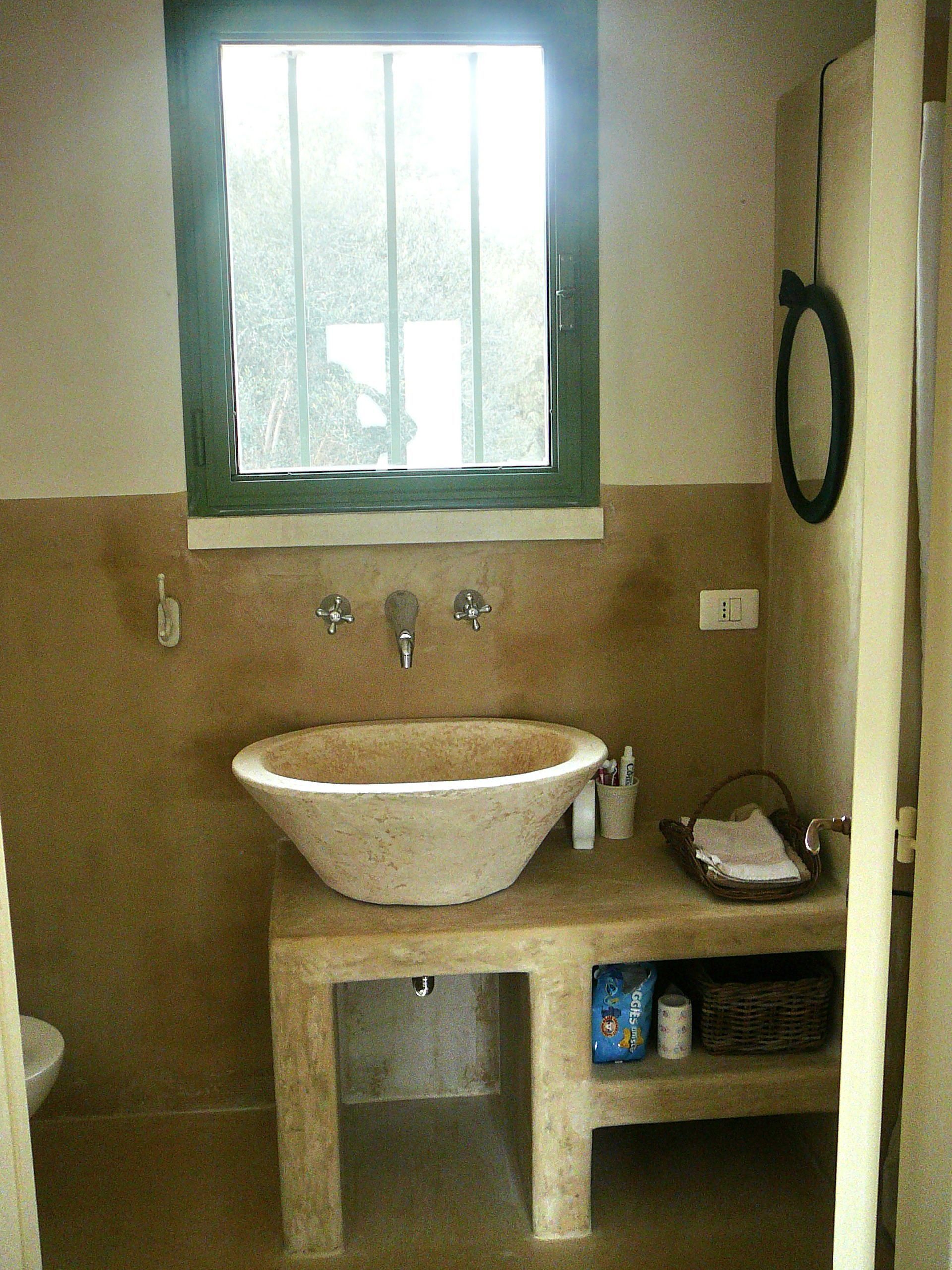 Une salle de bain avec un grand lavabo sur pied, une fenêtre au-dessus du lavabo, un porte-serviettes et une étagère contenant des articles de toilette.