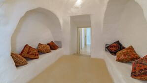 A narrow, arched room with white walls and a light-colored floor. There are several patterned cushions on the walls. - Raffinata dimora tipica tra ulivi, mandorli e fichi d'india (Ostuni)