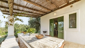 A covered outdoor dining area with a rustic wooden table, a woven basket, and a view of greenery. - Raffinata dimora tipica tra ulivi, mandorli e fichi d'india (Ostuni)