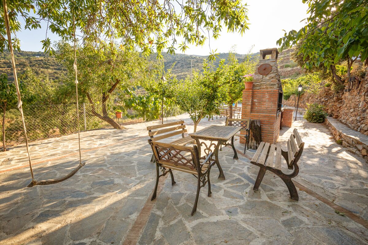 An outdoor patio with stone flooring, wooden benches, and a table.