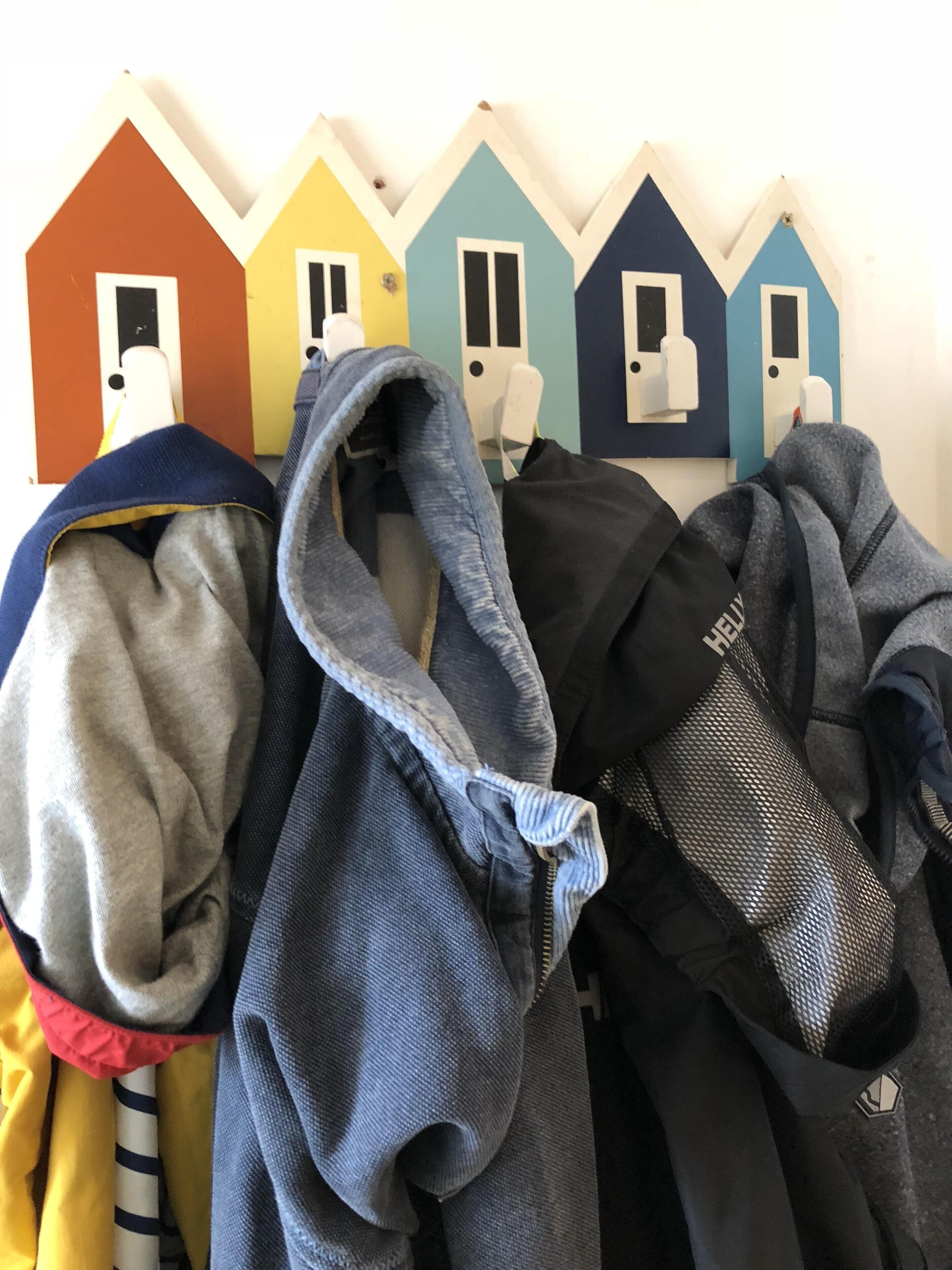 A row of colorful house-shaped hooks with various jackets and a backpack hanging on them.