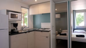 A compact kitchen with a microwave, stove, and sink. A bed is visible in the adjacent room. - Happy Camp in Camping Iscrixedda (Lotzorai)