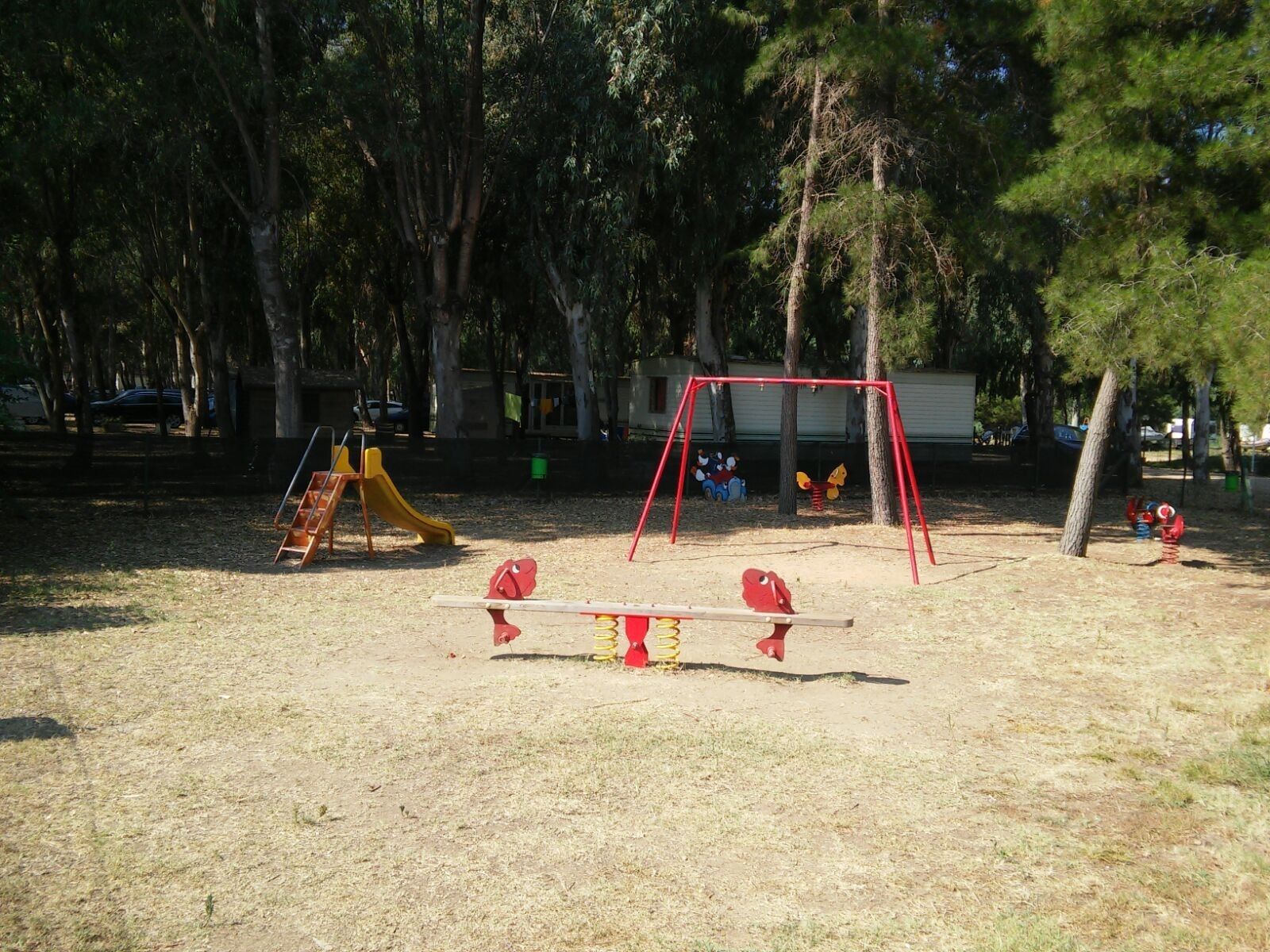 A playground with a swing set and a slide, surrounded by trees.