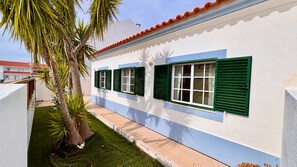 A building with a white exterior, green shutters, and a small lawn area with a palm tree.