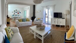Ein geräumiges Wohnzimmer mit einem weißen Sofa, einem weißen Couchtisch und einem Fernseher auf einem Schrank.