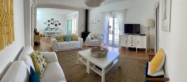 A spacious living room with a white sofa, a white coffee table, and a television on a cabinet.