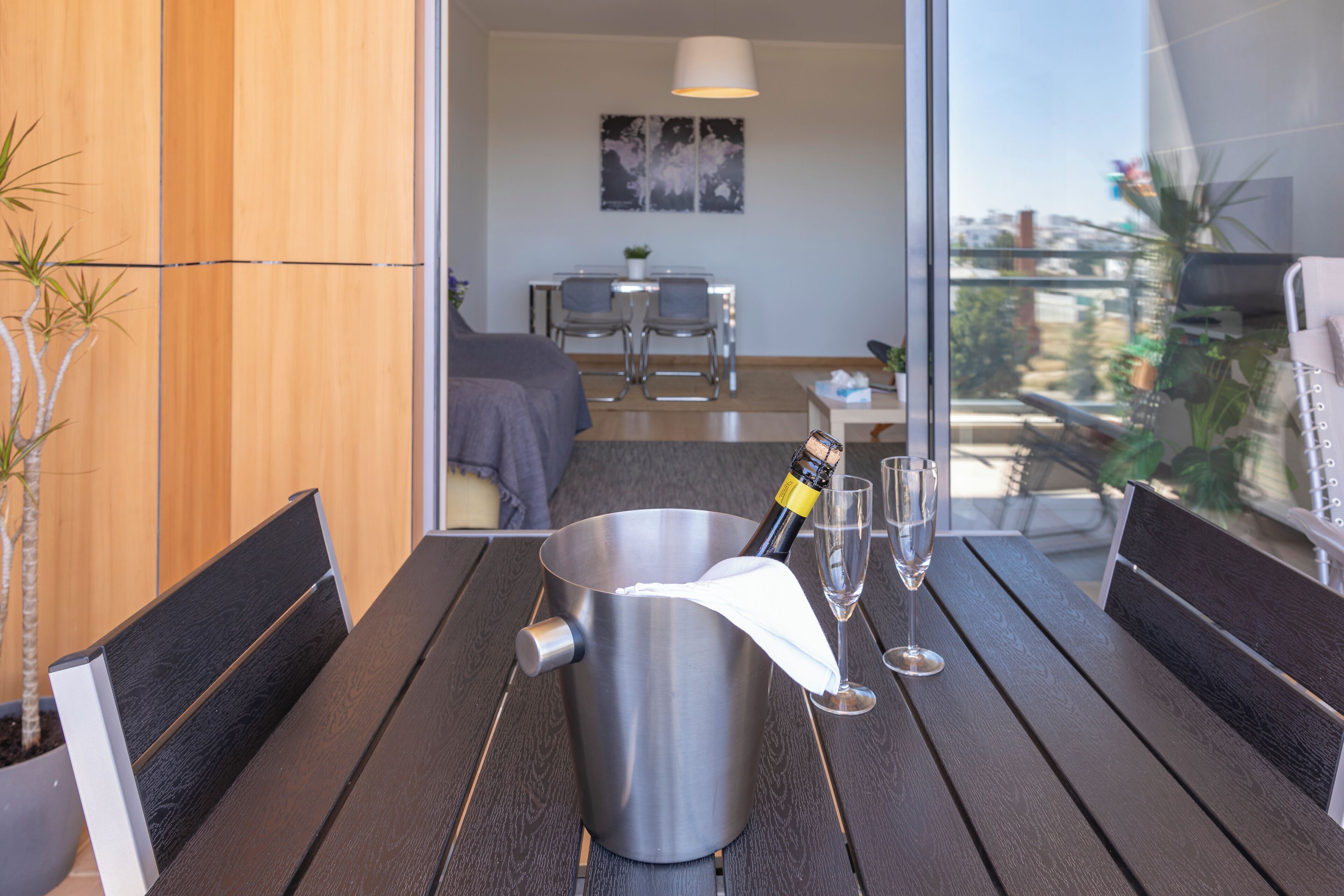 A modern room with a wooden wall, a dining table with chairs, a bed, and a balcony with plants.