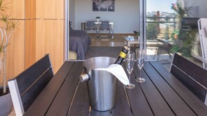 A modern room with a wooden wall, a dining table with chairs, a bed, and a balcony with plants. - Comfortable, cozy and comfy apartment by the Ria Formosa (Olhão)