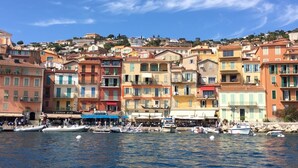 Un poble costaner amb edificis de colors, una marina amb vaixells i un cel blau clar.