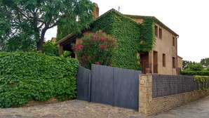 A house with a stone wall, a wooden gate, and a large tree. - House with garden and terrace, ideal to relax, near the Costa Brava (Monells)