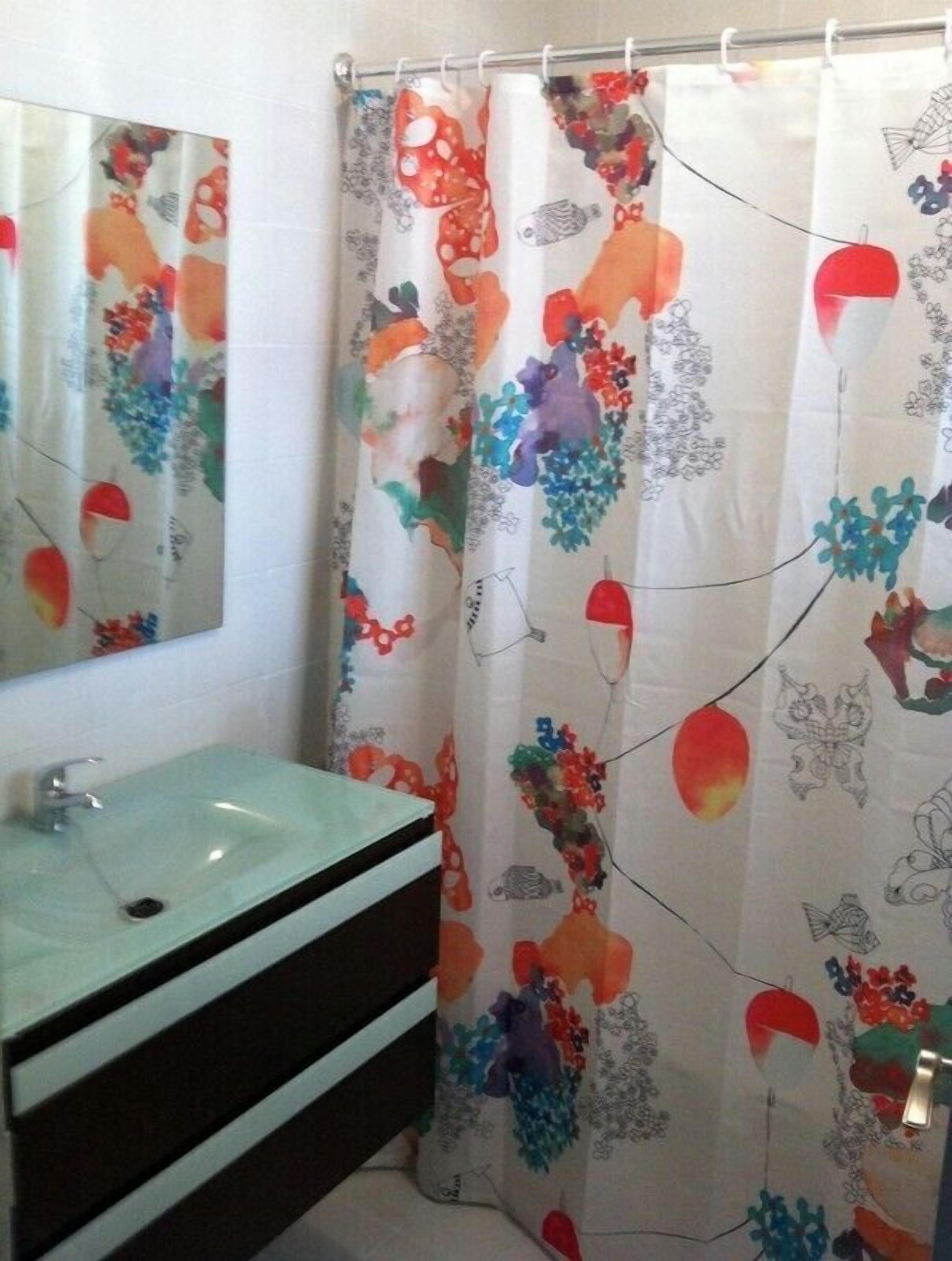 Un baño con lavamanos, espejo y cortina de ducha con estampado floral.