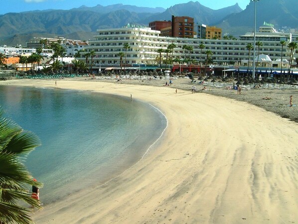 Una playa con un hotel al fondo, con varios pisos y balcones.