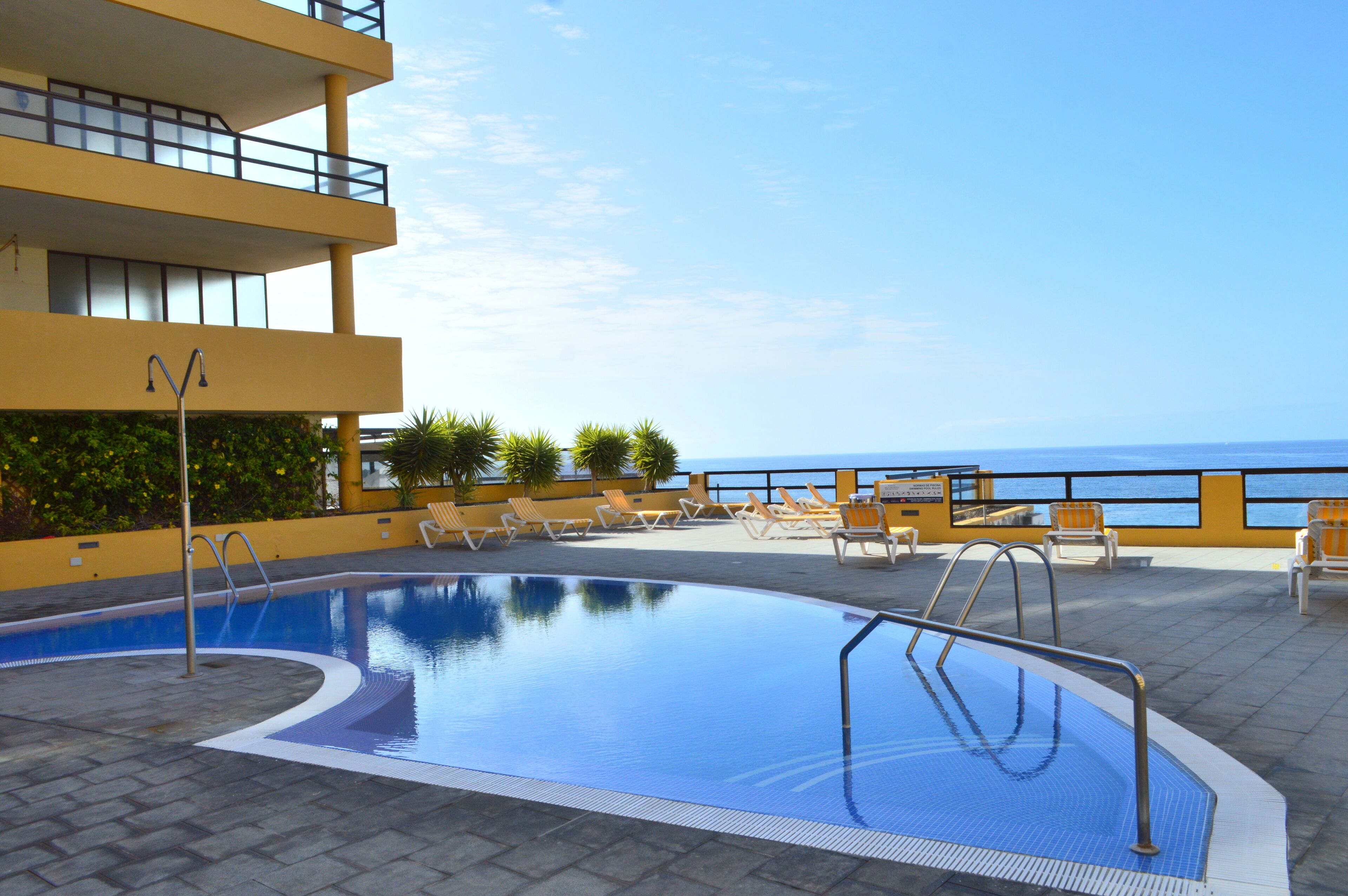Ein Pool auf dem Dach mit klarem, blauem Wasser, umgeben von Liegestühlen und Blick aufs Meer.