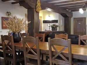 A dining area with a wooden table and chairs, a potted plant, and a kitchen in the background. - Casa Martikonea for 16 people (Basaburua)