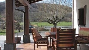 A covered patio with wooden furniture and a view of a tree and landscape. - Casa Martikonea for 16 people (Basaburua)