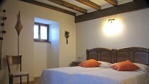 A bedroom with a wooden bed, two pillows, a nightstand, a chair, and a window. - Casa Martikonea for 16 people (Basaburua)