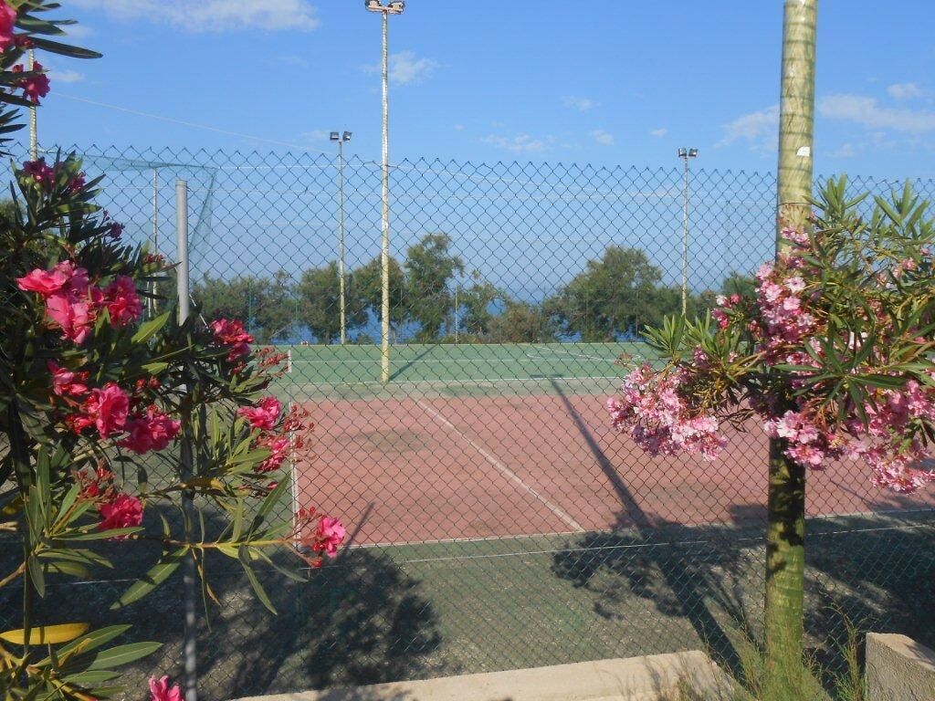 En tennisbane omkranset af et pigtrådshegn, med en klar himmel.