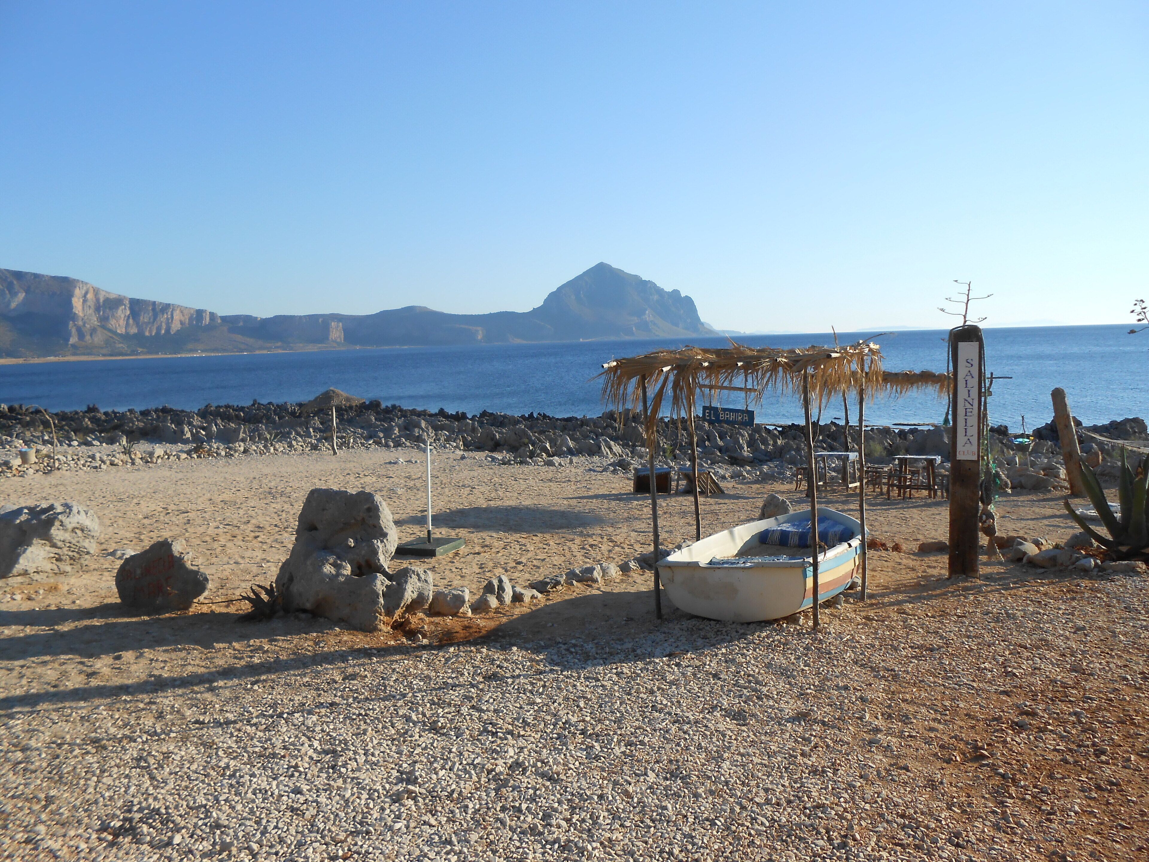 Ein Strand mit einem kleinen Boot, einer Holzkonstruktion und einem Schild mit der Aufschrift 'EL BAHIA'.