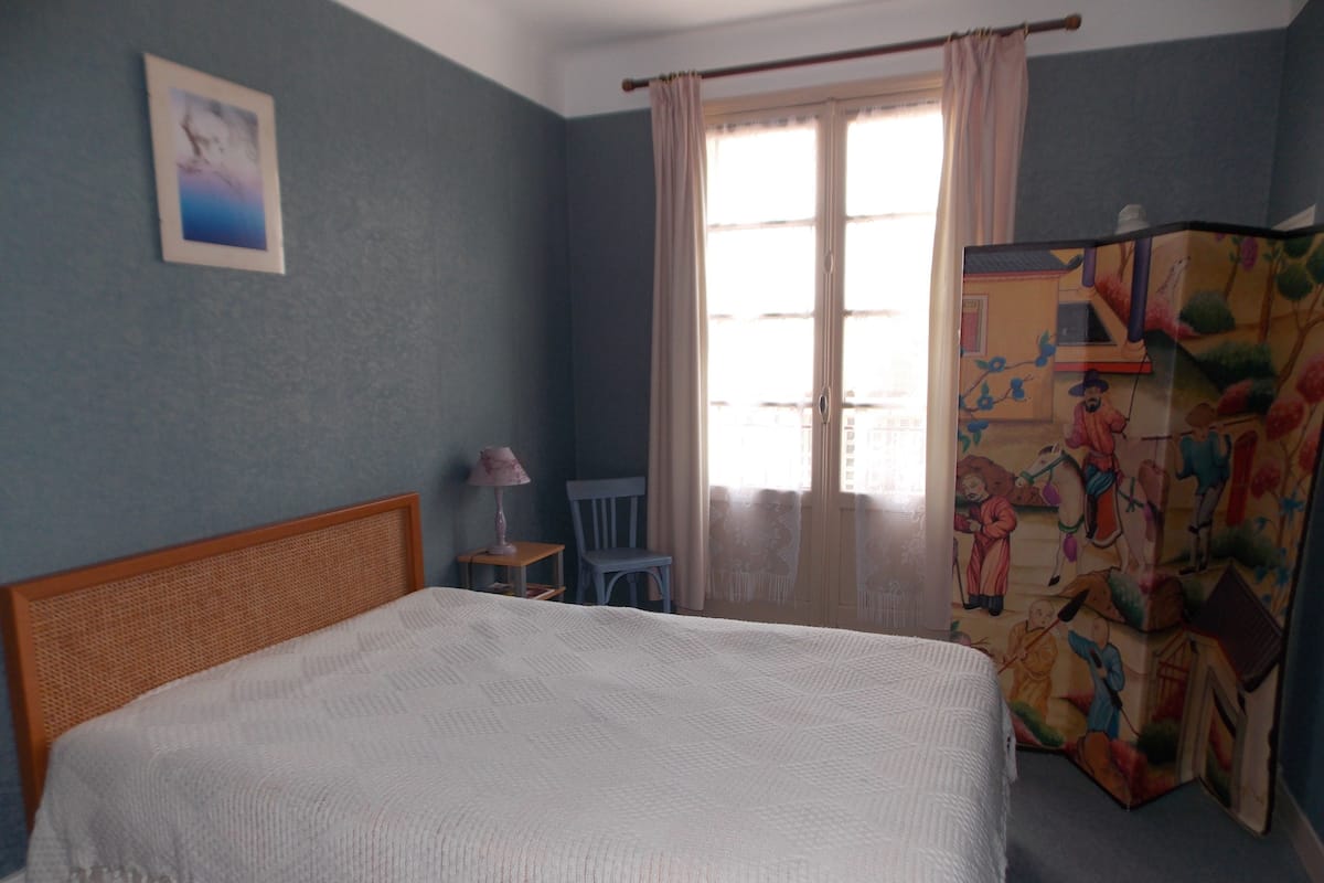 Un dormitorio con cama, una silla, una lámpara y una ventana con cortinas.