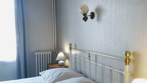 Ein ordentlich gemachtes Bett mit weißer Bettwäsche, ein Nachttisch mit Lampe und eine Wandleuchte.