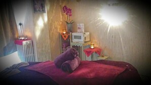 Ein Zimmer mit einem Bett, einem Heizkörper, einer Mikrowelle, einem kleinen Tisch mit Kerze und einem an der Wand befestigten Regal mit Pflanze.