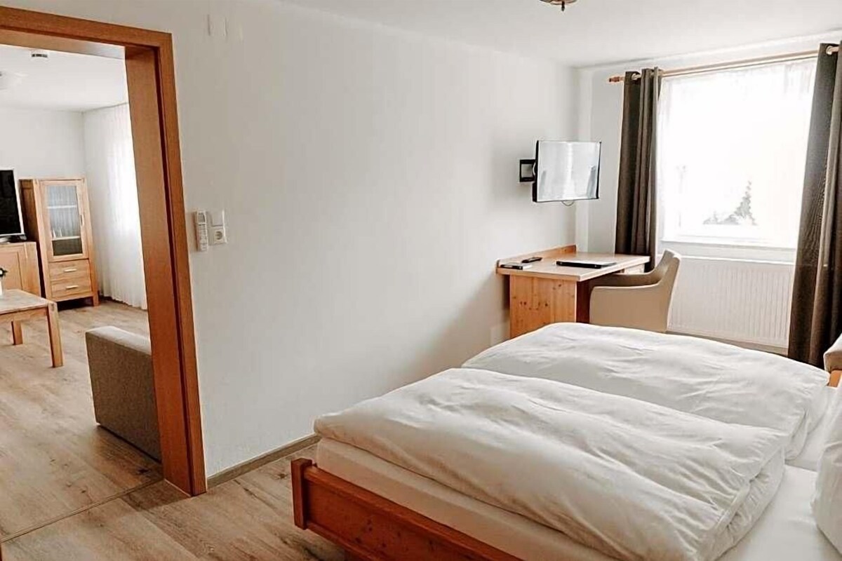 A hotel room with a bed, a desk, a chair, a lamp, and a window.