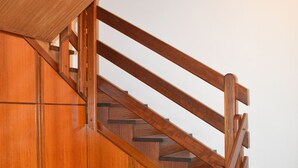 A wooden staircase with a handrail and a white vase on the floor.
