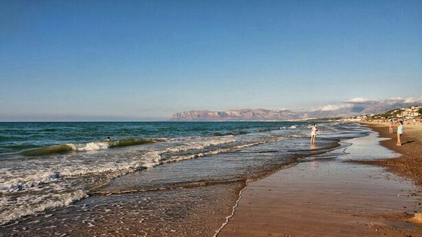 A beach with waves, a clear sky, and distant mountains.