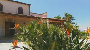 A building with a tiled roof and arched windows, surrounded by tropical plants and a clear sky.