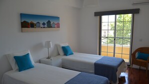 Hotellihuone, jossa on kaksi sänkyä, seinällä taulu, ikkunasta avautuva näkymä ja rottinkituoli.