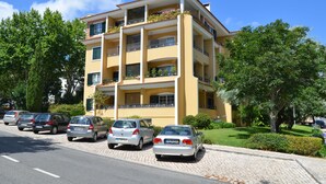 Monikerroksinen rakennus, jossa on parvekkeita, parkissa olevia autoja ja viheralueita.
