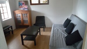 Uma sala de estar com um armário de madeira, uma cadeira preta, um sofá cinza com almofadas pretas e uma mesa de centro de madeira.