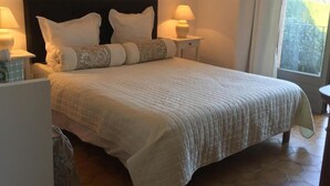 Ein Schlafzimmer mit einem großen Bett, zwei Nachttischlampen, einem Nachttisch und einem Fenster mit Vorhängen.