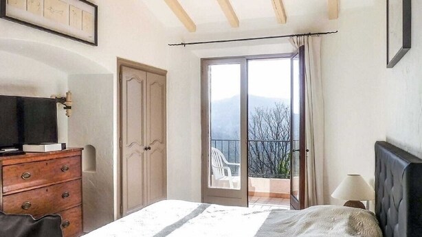 Ein Schlafzimmer mit Bett, Kommode, Fernseher und einem Balkon mit Blick auf Bäume und Berge.