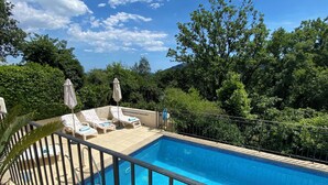 Ein rechteckiger Pool mit einer gefliesten Kante, umgeben von einem Metallgeländer. Am Poolufer stehen Liegestühle und Sonnenschirme.