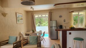 A cozy living area with a dining table, chairs, a sofa, and a kitchen area with a refrigerator and bar stools. - Charming 3 bedroom villa with pool, only 4 minutes walk to amazing beach (Mont Choisy)