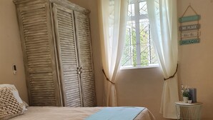 A bedroom with a bed, a window with curtains, a wall-mounted air conditioner, and a small table with a plant. - Charming 3 bedroom villa with pool, only 4 minutes walk to amazing beach (Mont Choisy)