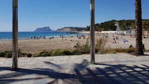 A beach with a wooden pergola structure, stone pavement, and palm trees. - Villa Ra - Enchanting Moraira Villa with Secluded Pool and Sea View      (Alicante)