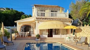 A two-story house with a swimming pool, outdoor seating, and a view of the surrounding landscape. - Villa Ra - Enchanting Moraira Villa with Secluded Pool and Sea View      (Alicante)