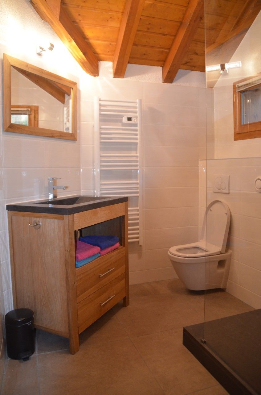 Ein Badezimmer mit einem Holzkosmetikschrank, einer Toilette und einer Duschkabine aus Glas.