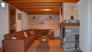 A cozy living room with a wooden ceiling, a stone fireplace, and a sofa with cushions. - Luxury chalet SKI-IN / SKI-OUT. Free wifi, sauna and beautiful view !!! (Oz)