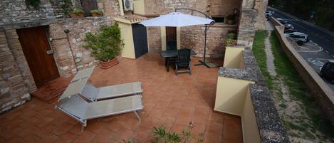 A patio with two lounge chairs, a table, and an umbrella. There is a brick wall and a stone archway in the background.