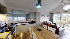 A modern kitchen with a wooden dining table, white chairs, and a built-in oven. - Blue Anchor Retreat -  a beach house that sleeps 4 guests  in 2 bedrooms (Filey)