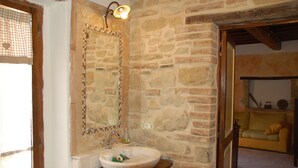 A rustic bathroom with a stone wall, a wooden vanity, a large mirror, and a light fixture.