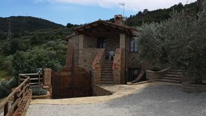 A stone building with a wooden door and steps leading up to it, surrounded by gravel and greenery.